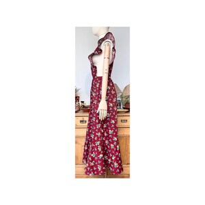 May include: A burgundy maxi dress with a floral pattern. The dress features a ruffled neckline and a tiered skirt. The dress is displayed on a mannequin. The floral pattern includes blue, yellow, and white flowers.