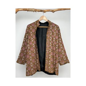 Könnte beinhalten: Eine braune und rosafarbene gemusterte Jacke mit schwarzem Futter. Die Jacke hat einen Stehkragen und einen Knopfverschluss.