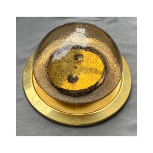 May include: A decorative glass bowl with a gold-colored base. The bowl is a dark, smoky color with a gold-colored design inside. The base is a wide, circular shape with a shiny, metallic finish. The bowl is likely used for decorative purposes.