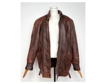 May include: A brown leather jacket with a zip-up front, two front pockets, and a collared neckline. The jacket has a two-tone design with darker brown accents on the shoulders and sleeves. The jacket is displayed on a mannequin.