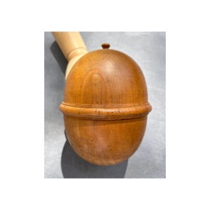 Peut inclure: Un récipient en bois en forme de gland, avec un dessus arrondi et une base. Le récipient est en bois brun clair et possède un petit bouton sur le dessus. La base est ornée d'un anneau décoratif.