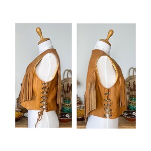 May include: A brown leather vest with fringe detailing and a lace-up front. The vest has a suede lining and is a vintage style.