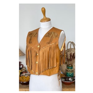 May include: A brown leather waistcoat with fringe and gold studs. The waistcoat has a decorative design on the front with two stylised shapes.