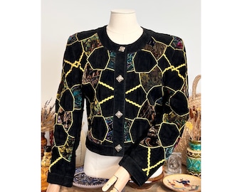 May include: Black suede jacket with a unique patchwork design. The jacket features geometric shapes in various colors and textures, outlined with yellow stitching. It has a round neckline and decorative buttons.