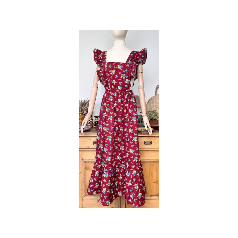 May include: A burgundy floral print dress with a square neckline and ruffled cap sleeves. The dress features a fitted waist and a flared skirt with a ruffle hem. The fabric is patterned with small blue and yellow flowers.