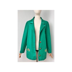 May include: A green corduroy jacket with a satin collar and decorative buttons. The jacket has two pockets with embroidered floral details.