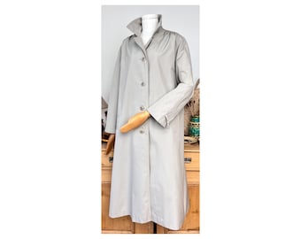 May include: A long, light gray trench coat with a button closure and a collar. The coat has a simple design and is made of a smooth fabric.