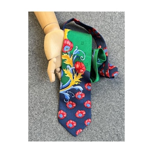 May include: A necktie featuring a vibrant green and dark blue background with a repeating pattern of red poppy flowers, blue centers, and yellow leafy scrollwork. The tie displays a distinct color-blocked design with a green upper section.