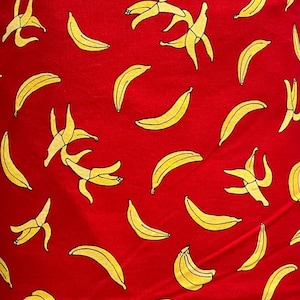 May include: Red fabric with a repeating pattern of yellow bananas and banana peels. The bananas are in various stages of being peeled, with some whole and others partially exposed.