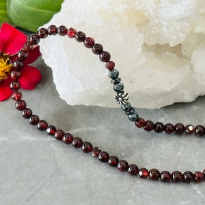 May include: A red garnet gemstone bracelet with a silver charm and black hematite beads.