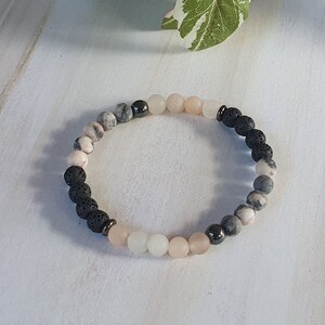 May include: A beaded bracelet featuring black lava rock, pink and grey agate, and silver beads.