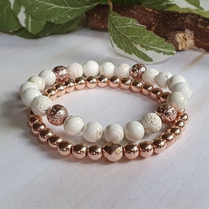 May include: Two bracelets, one with white lava rock and white beads, and the other with rose gold beads.