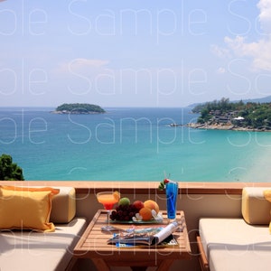 May include: A balcony with two white couches and yellow pillows overlooking a beach and ocean. A small wooden table with a glass of orange juice and a plate of fruit sits in the center of the balcony.