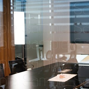 Puede incluir: Una vista a través de una pared de vidrio hacia una sala de conferencias con una mesa larga de madera oscura y sillas. Un trozo de papel con un gráfico está sobre la mesa.