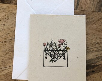 May include: A card with a hand-drawn illustration of a white envelope filled with colorful flowers. The card is made of recycled paper and has a natural, rustic look.