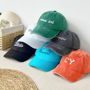 以下が含まれることがあります： 黒、白、緑、青、オレンジなど、さまざまな色の野球帽のコレクション。各キャップには、「Silivia」、「Beautiful」、「custom text」などの白い刺繍が施されています。キャップはカジュアルに積み重ねられています。