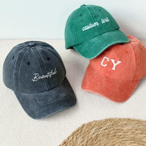 May include: Three baseball caps in different colors: a dark gray cap with the word "Beautiful", a green cap with "custom text", and a coral cap with "CY". The caps are made of a soft, worn fabric.