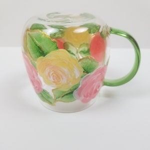 May include: A clear glass mug with a green handle, hand-painted with pink, yellow, and green roses.