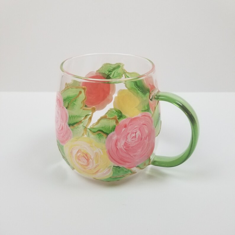 May include: A clear glass mug with a green handle, painted with pink, yellow, and orange roses and green leaves.