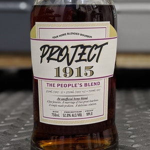 May include: A clear glass bottle of bourbon with a label that reads "PROJECT 1915 THE PEOPLE'S BLEND." The label includes text about the blend and the alcohol content. The bottle is sealed with a black cap and a purple strip that says "Blended at Home." The bottle contains 750ml.