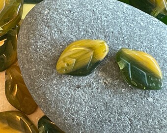Op de afbeelding: Twee groene en gele tijgeroogstenen, een met een meer uitgesproken groene tint, op een grijze steen.