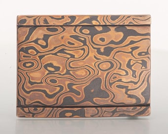 May include: A rectangular box with a unique pattern. The box features a swirling design in shades of brown and black, creating a marbled effect. The box has a smooth, polished finish and a simple, elegant design.