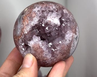 Puede incluir: Una esfera de amatista púrpura con una gran geoda abierta en su interior. La geoda está llena de cristales de amatista más pequeños y brillantes.