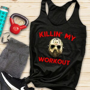 Puede incluir: Camiseta sin mangas negra con el texto "KILLIN' MY WORKOUT" en rojo y una máscara de hockey. La imagen también incluye leggings grises, una zapatilla negra, una pesa rusa roja y una botella de agua.