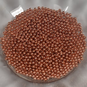 May include: A large quantity of small, round, copper-colored beads. The beads are arranged in a circular pattern and appear to be made of metal.