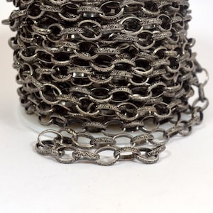 May include: A close-up of a silver chain with an ornate design. The chain is coiled up on a spool.