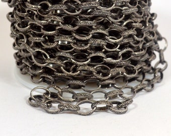 Könnte beinhalten: Nahaufnahme einer silbernen Kette mit einem verzierten Design. Die Kette ist auf einer Spule aufgewickelt.