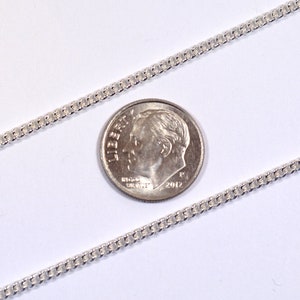 May include: A silver chain necklace with a delicate, rounded link pattern. The chain is laid out on a white surface next to a US dime for scale.