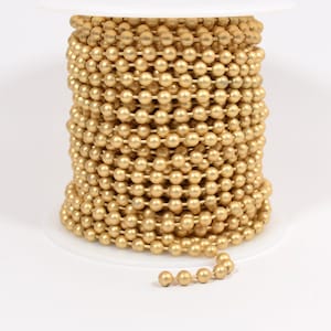 May include: A spool of gold-colored chain with round links. The chain is wound around a white spool.
