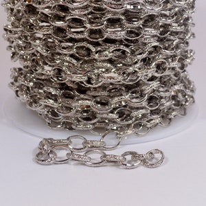 May include: A close-up of a silver chain with a textured finish. The chain is coiled on a spool and a small section is laid out straight.