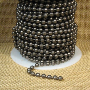 May include: A spool of gunmetal gray ball chain. The chain is made of metal beads and is approximately 1/4 inch in diameter. The chain is wound around a white spool.