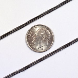 May include: A black chain necklace with a curb link style. The chain is laid out on a white surface next to a US dime coin for scale.