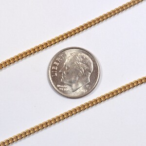 May include: A gold chain necklace with a curb link style. The chain is laid out on a white surface next to a US dime for scale.