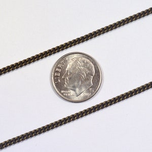 May include: A close-up of a dark brown chain next to a US dime coin. The chain is about the same width as the coin.