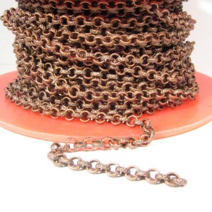 May include: A spool of copper-colored chain with a textured finish. The chain is wound around a pink spool and a small section of the chain is laid out straight on a white surface.