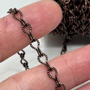May include: A close-up of a copper chain with a textured finish. The chain is made of small, oval-shaped links.