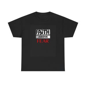 以下が含まれることがあります： 「FAITH ABOVE FEAR」の文字が白と赤でデザインされた黒いTシャツ。テキストはTシャツの前面の中央に配置されています。Tシャツは柔らかい素材で作られています。