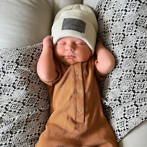 infant wearing cream beanie with personalized gray patch and aged brass rivets