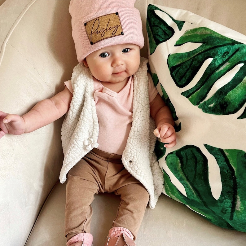 infant wearing light pink beanie with personalized cork patch and matte black rivets