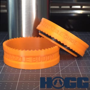 May include: Two orange plastic rings with the words "Puzzle Buddy" and "Puzzle Guide" printed on them. The rings are designed to fit around a water bottle.