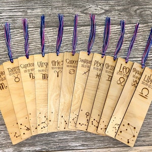 May include: Twelve wooden bookmarks featuring zodiac signs and dates. Each bookmark has a constellation design and a blue and purple tassel.