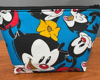 May include: A blue cosmetic bag featuring a repeating pattern of cartoon characters with black, white, red, and yellow accents. The bag has a black zipper closure and is made of fabric.