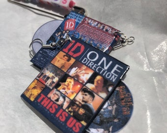 May include: Handmade earrings featuring miniature DVD covers and a CD with the text "One Direction". The earrings include a safety pin with the word "THREADS" spelled out in colorful beads. The DVD covers display images of the band.