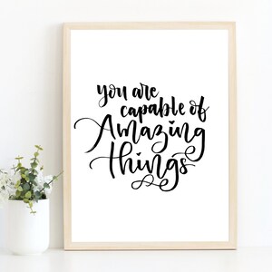 May include: A framed print with a white background and black calligraphy that reads "You are capable of amazing things."