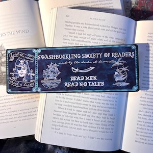 May include: A rectangular bookmark with a pirate theme. It features a pirate illustration, a ship, and the text "SWASHBUCKLING SOCIETY OF READERS" and "DEAD MEN READ NO TALES" on a blue background.