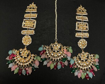 May include: A gold and white Indian bridal jewelry set with a maang tikka, earrings, and a necklace. The set features intricate designs with colorful beads and stones.